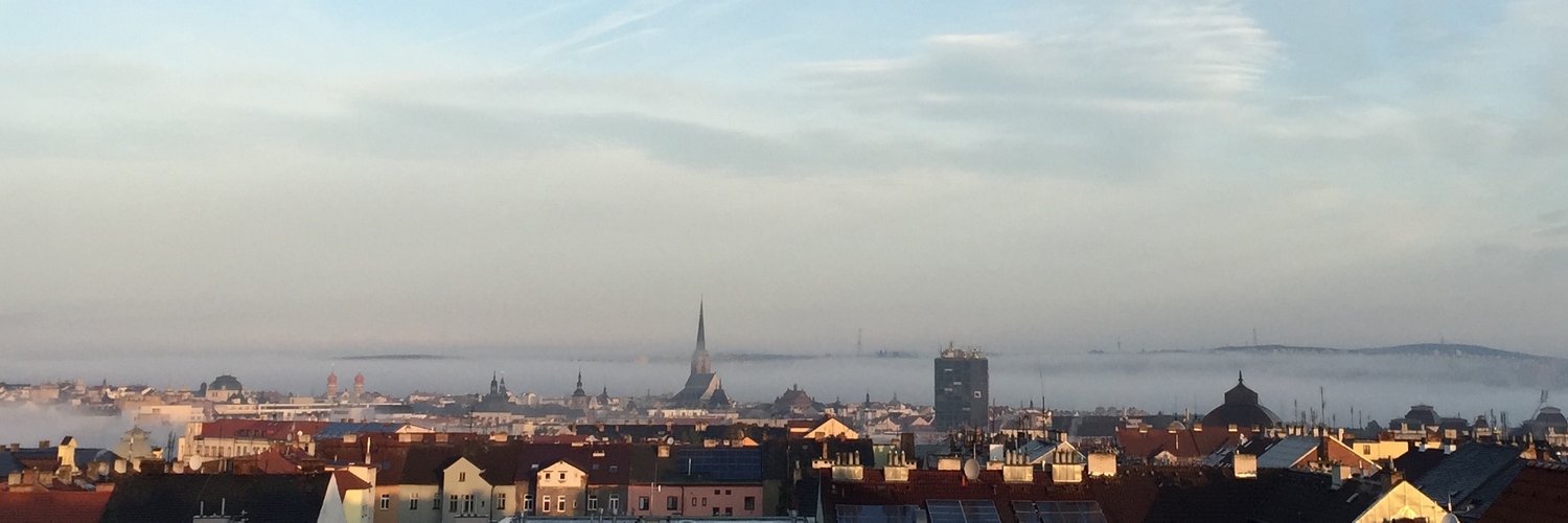 Rooftops of Pilsen and a church spire rising out of morning fog